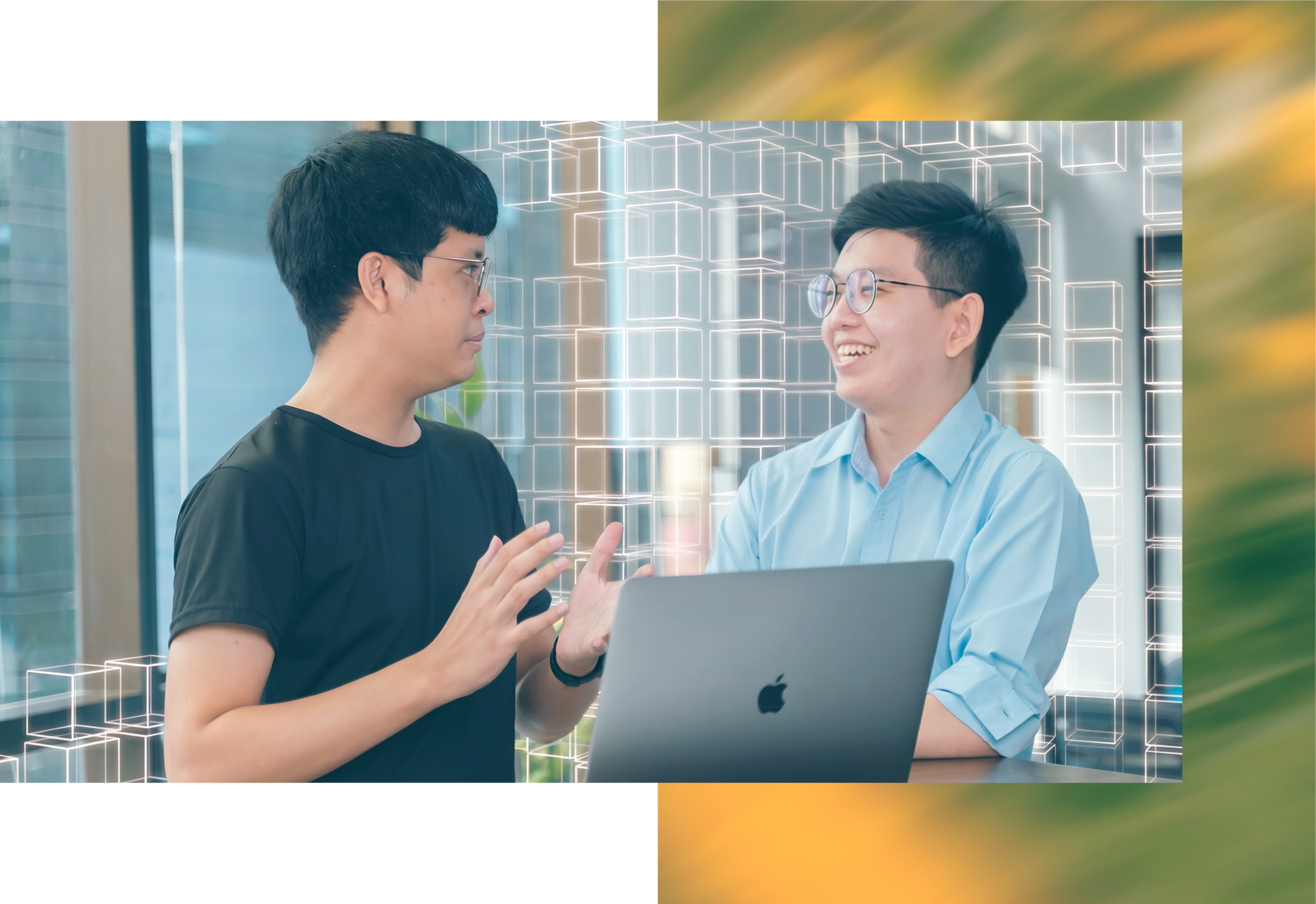 Two of our Thai colleagues, deep in discussion across a laptop. One is laughing and they have an office behind them with cubes