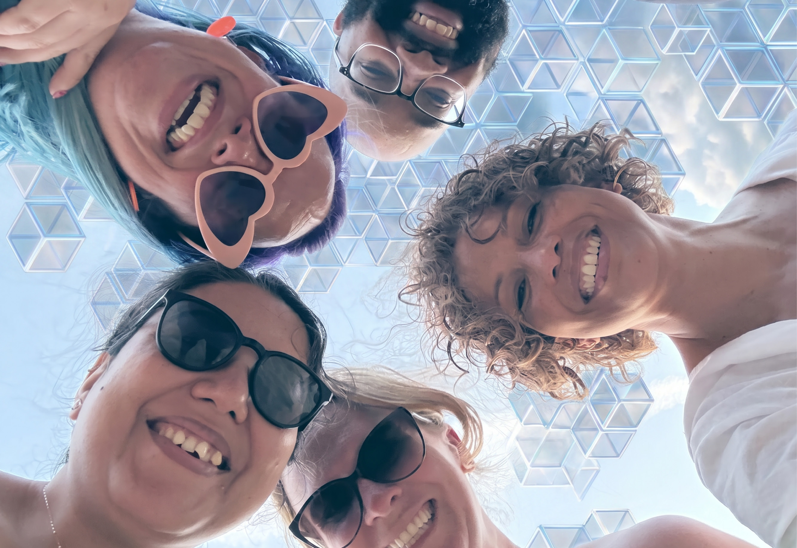 A fun team shot - everyone is in a circle looking down at the camera, smiling with the sky behind them made of AI cubes