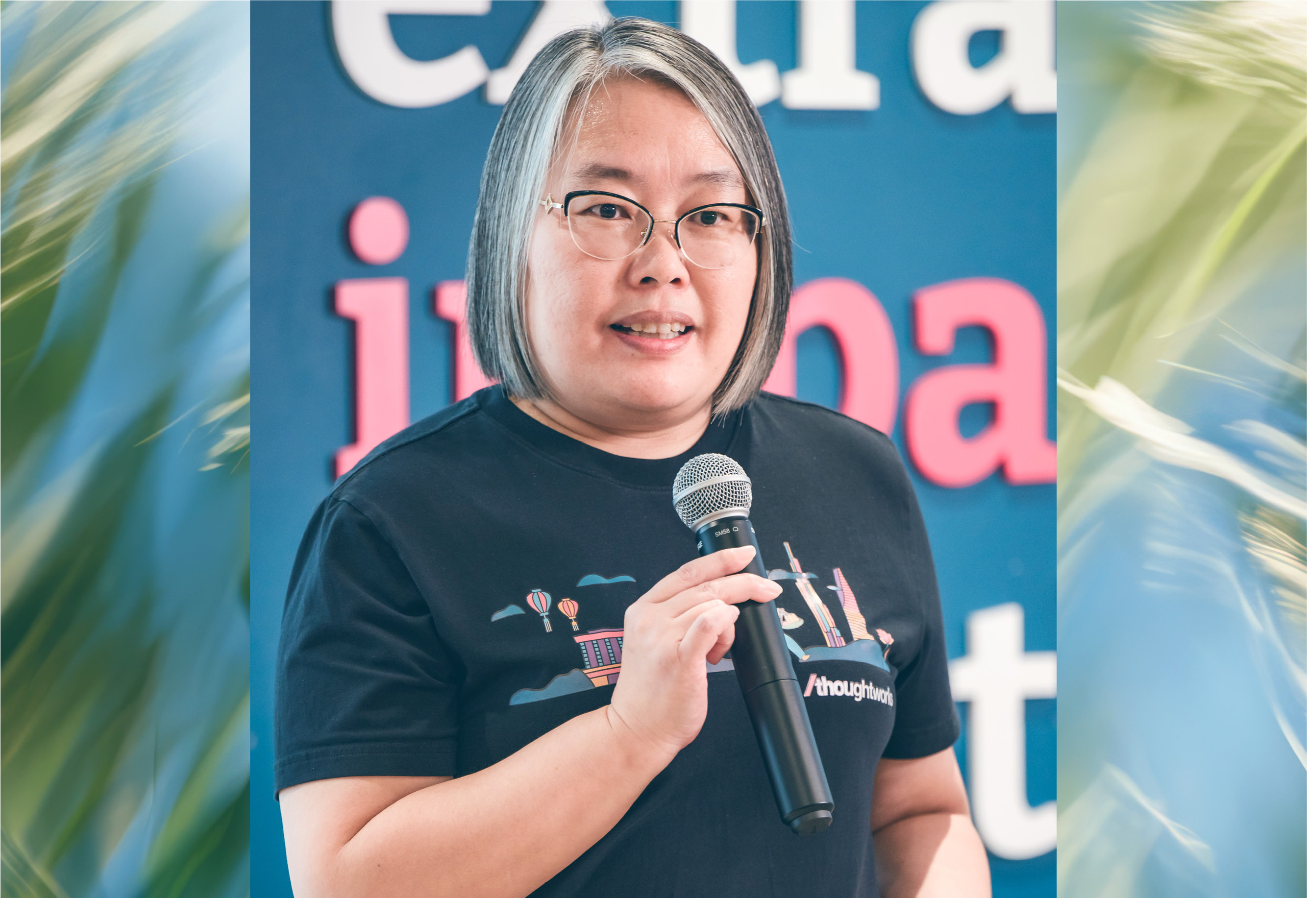Photo of a Thoughtworker on stage at xConf, she is of Asian heritage, with short grey hair and glasses, wearing a Thoughtworks tee