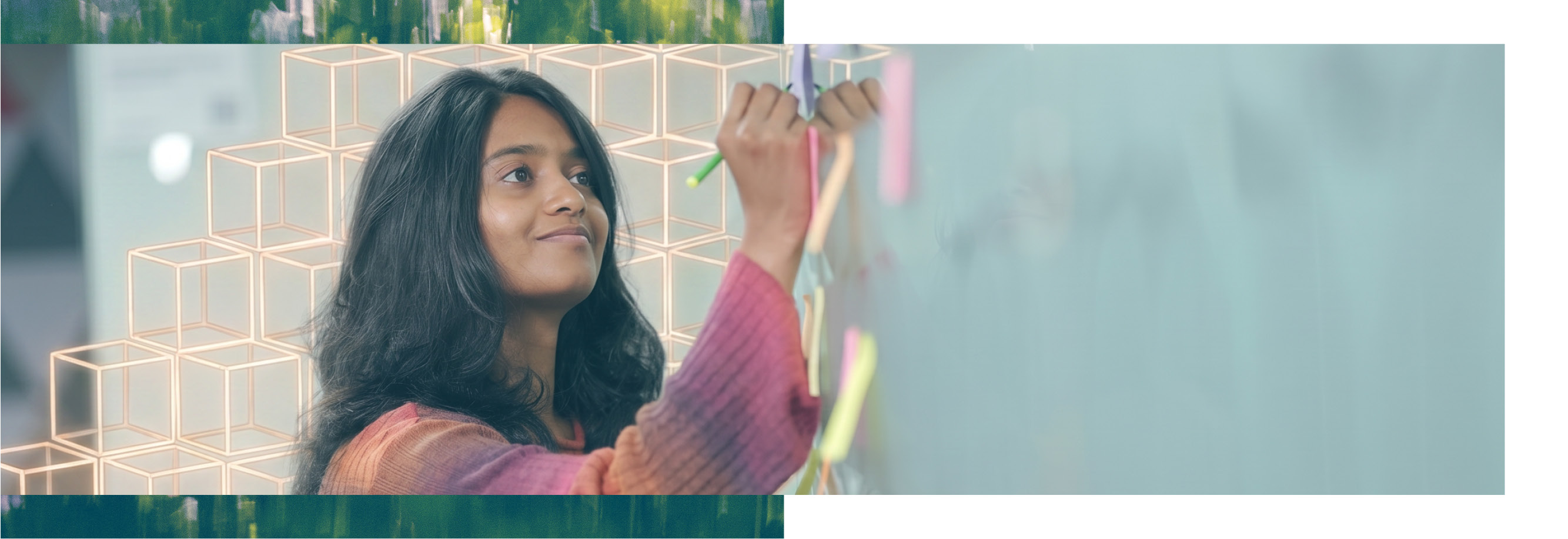 Wearing a multicoloured top, this Thoughtworker is smiling to herself while she writes on a sticky on the wall. AI cubes are in the background.