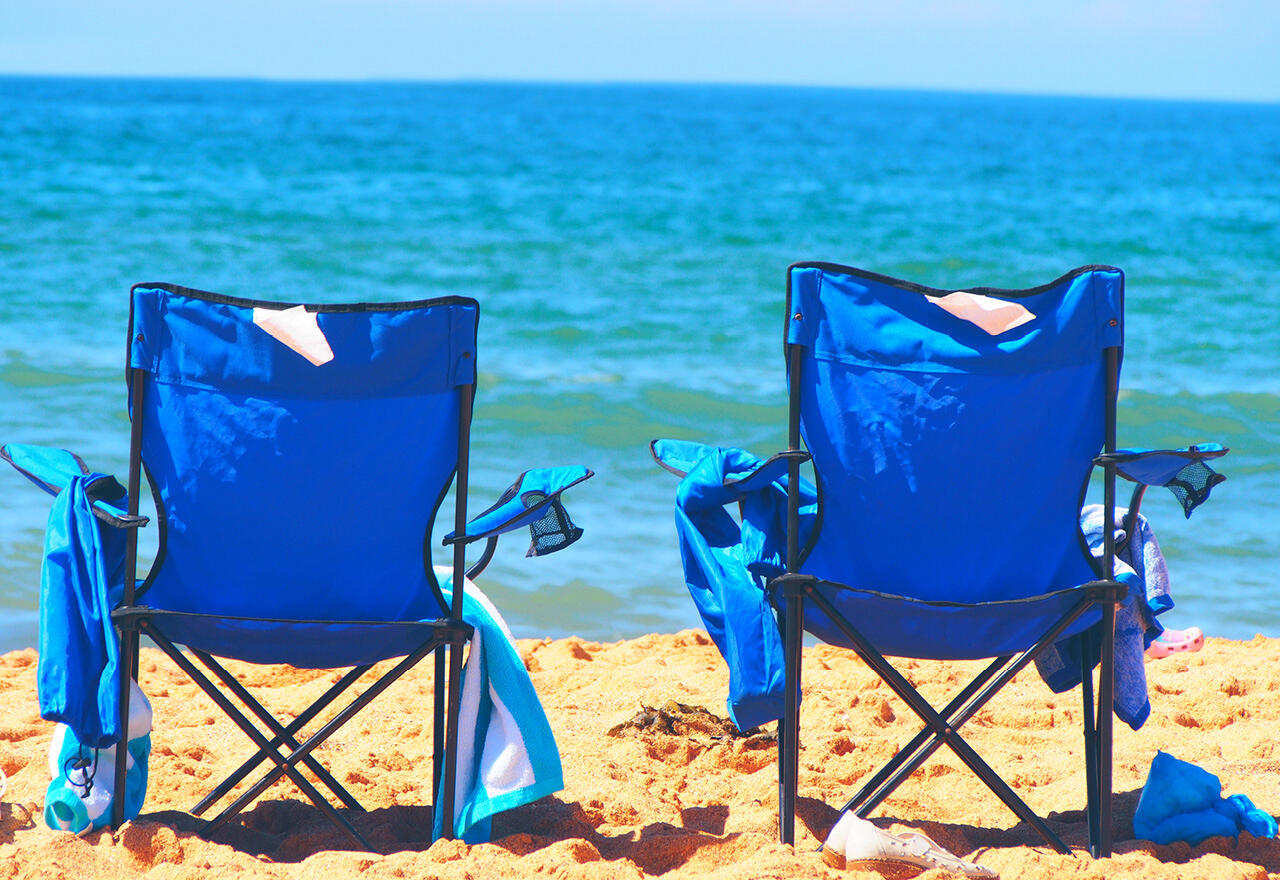 two blue beach chairs on a beach overlooking the ocean