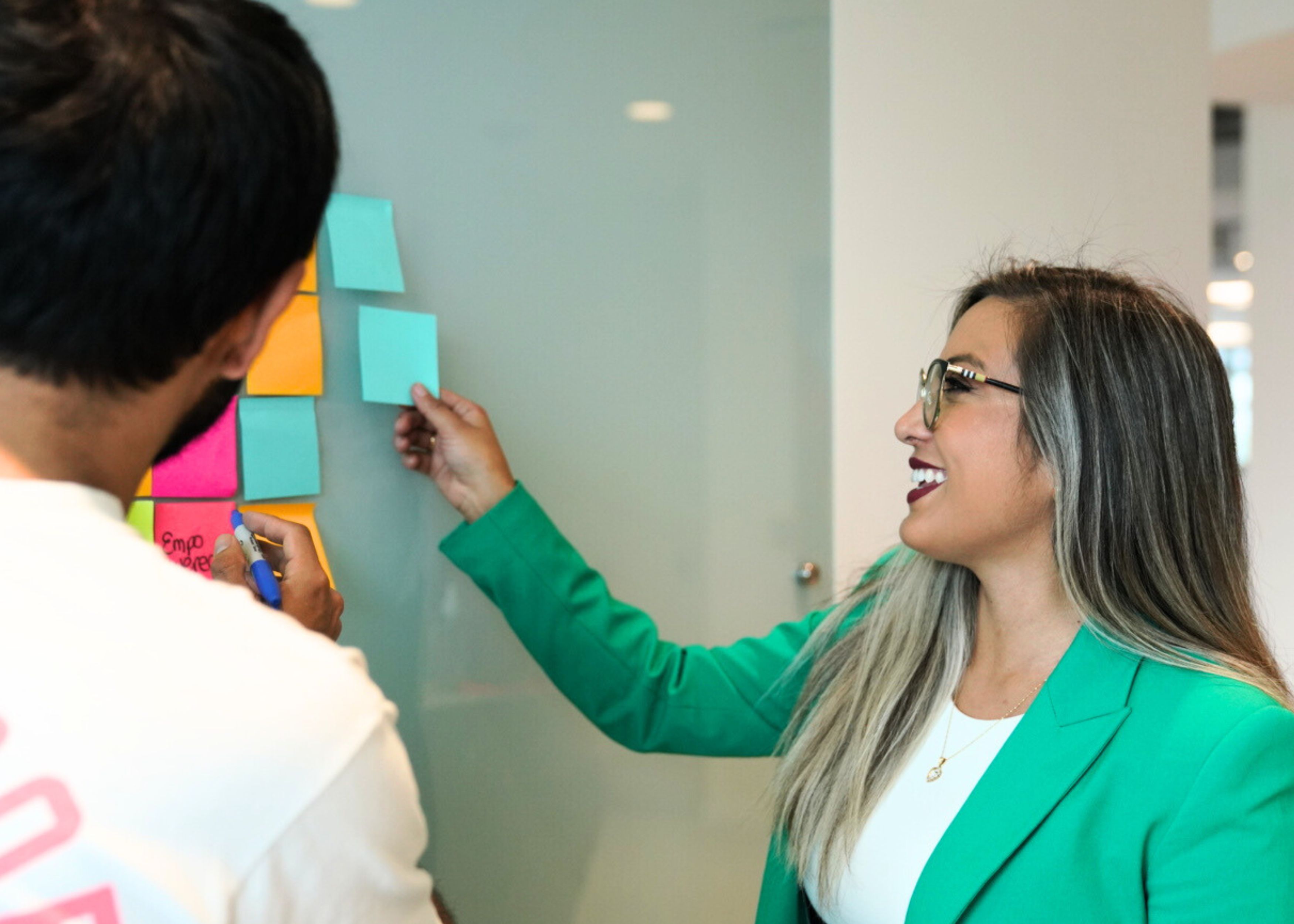 Two people working with Post-it notes attached to a glass wall