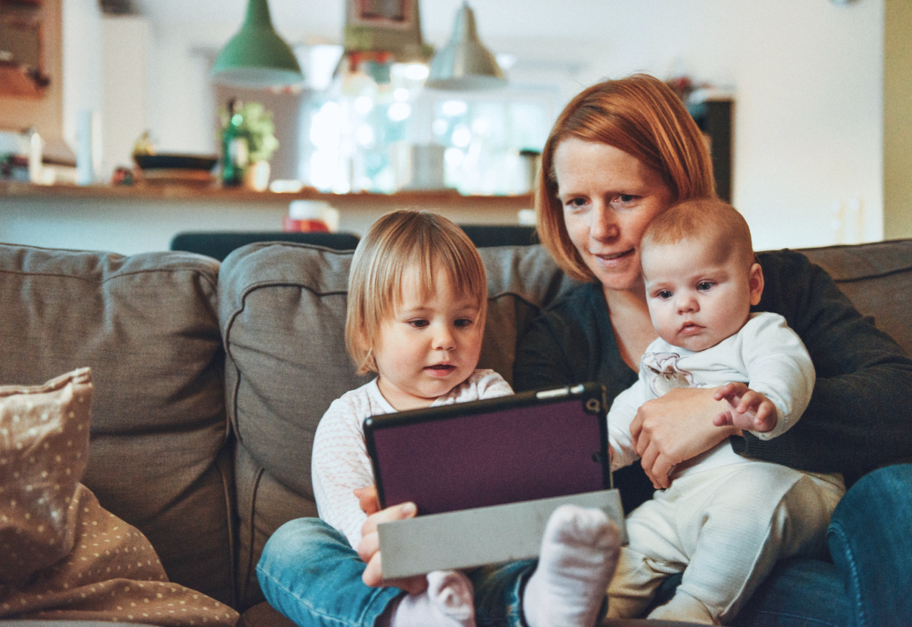 A mother and her two young children looking at a tablet.