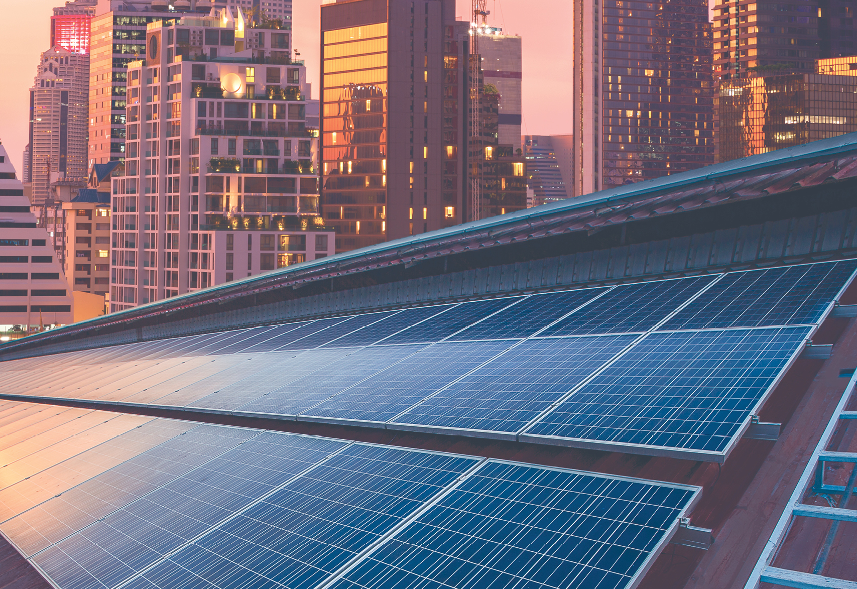 Solar pannels over a rooftop in a sunset with a city landscape on the background