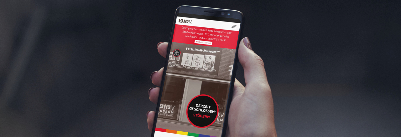 A hand holding a mobile phone displaying the FC St. Pauli Museum app