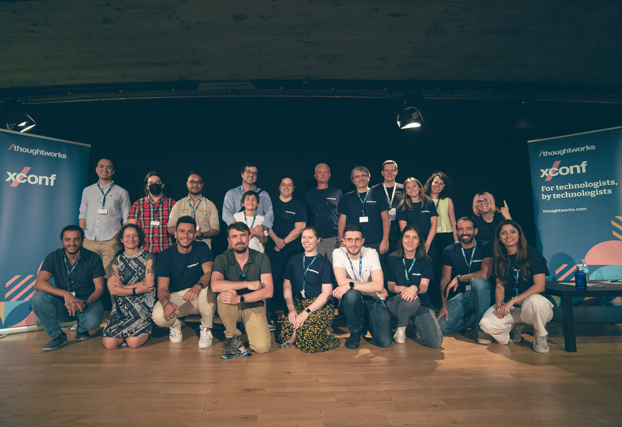 Group of XConf Europe 2022 event speakers and organizers standing on stage between two branded pop up banners
