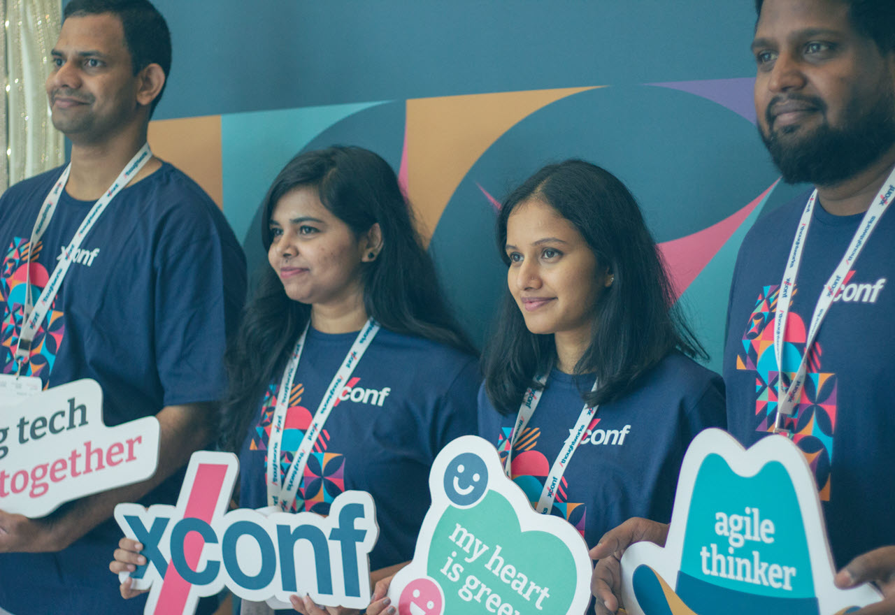 A team of four Thoughtworkers in XConf tshirts pose for photo, each holding a photo prop sign