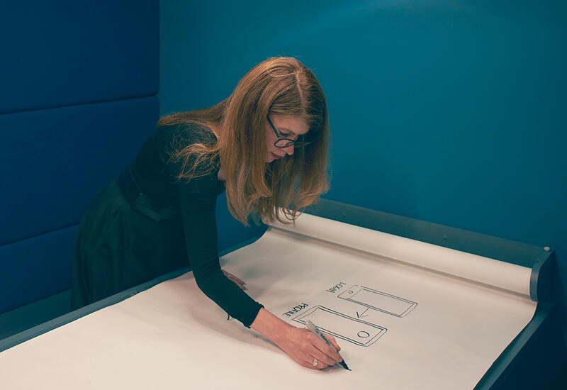 A woman sketching mobile wireframes on a large sheet of paper