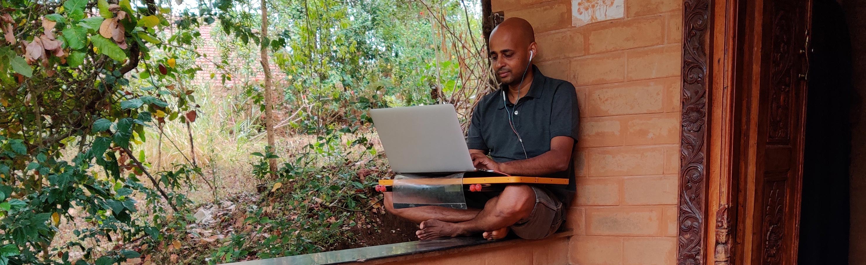 Photo of a man sitting on his porch, working on a laptop in remote India