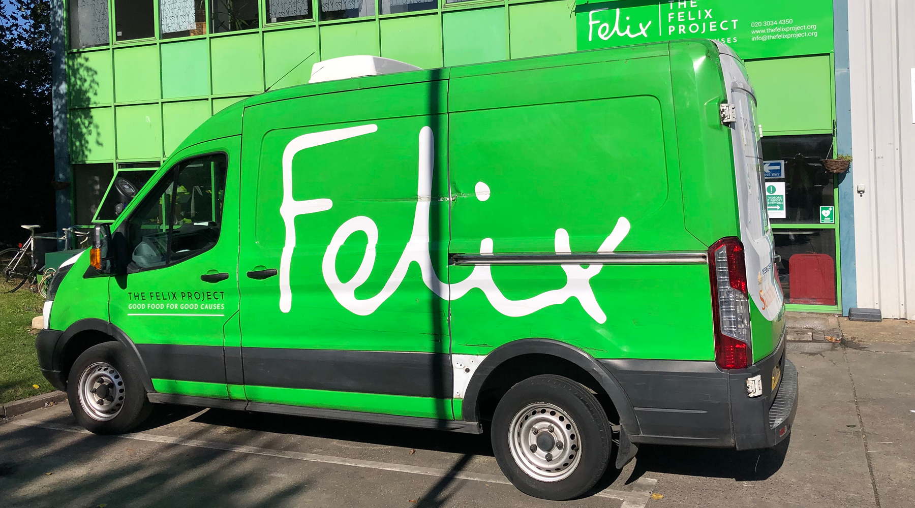 Green van Bright green Felix van with the name written over one side and a volunteer wearing a high visibility jacket and a green top loading donated goods into the van