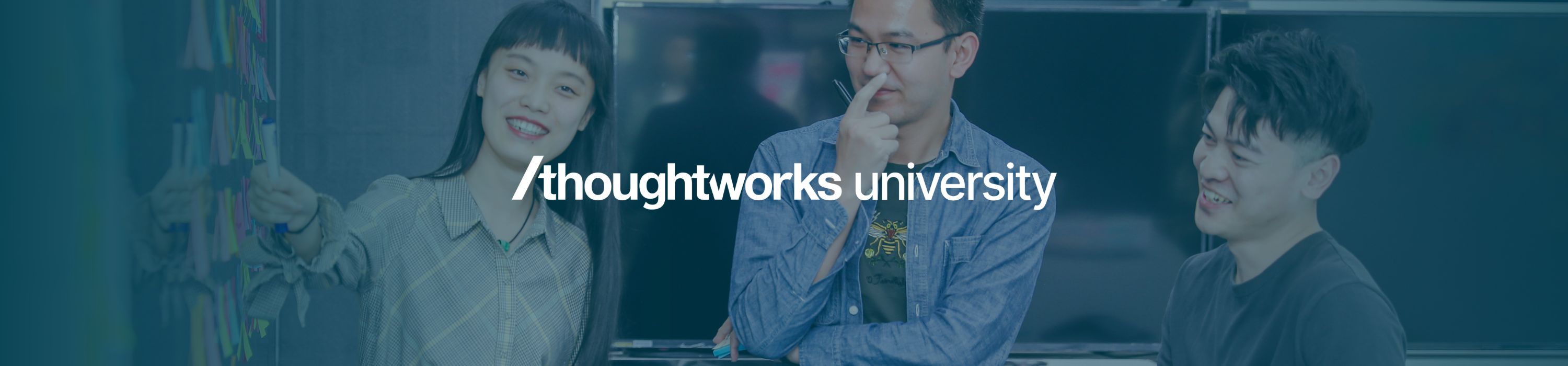 Group of Thoughtworkers in front of a blue wall featuring the Thoughtworks University logo in bold white text.