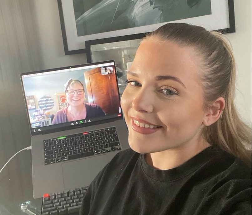 Image of Ella smiling taking a selfie of her and behind her is a Zoom screen with an image of her mentor on the screen. They are on Zoom together. 