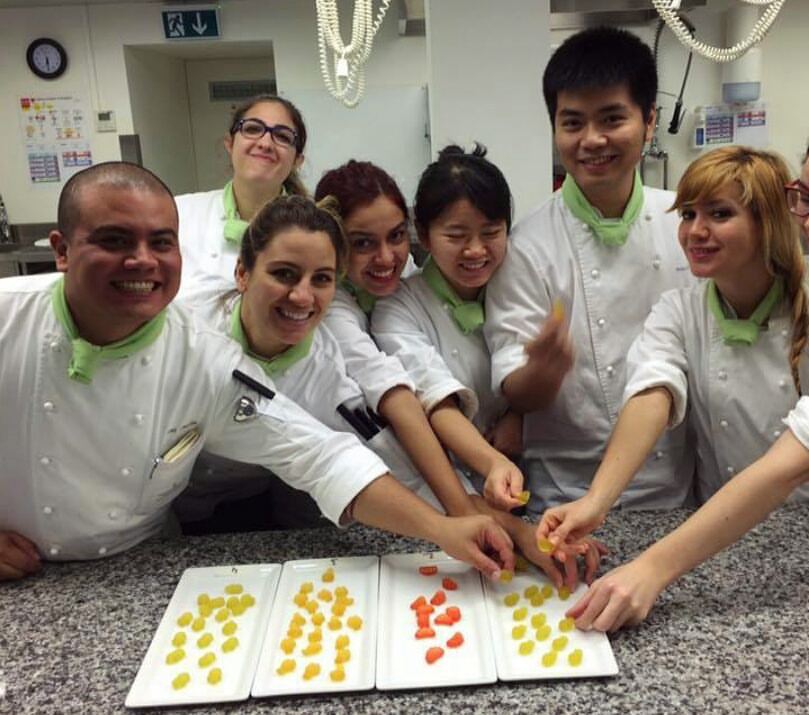 Image of 7 people in a kitchen, wearing chefs uniform