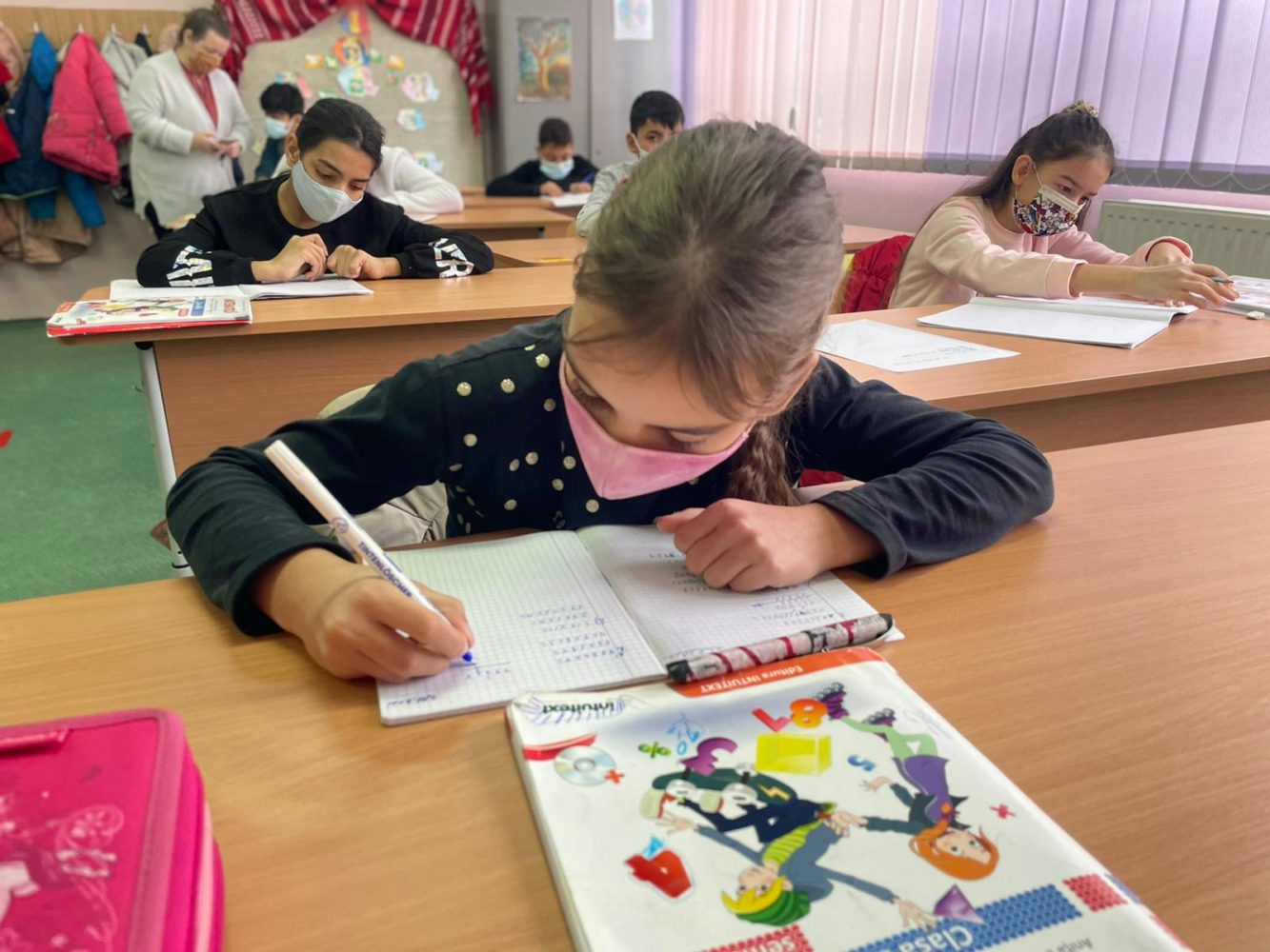 Image of a child in a classroom. The child is writing on a workbook