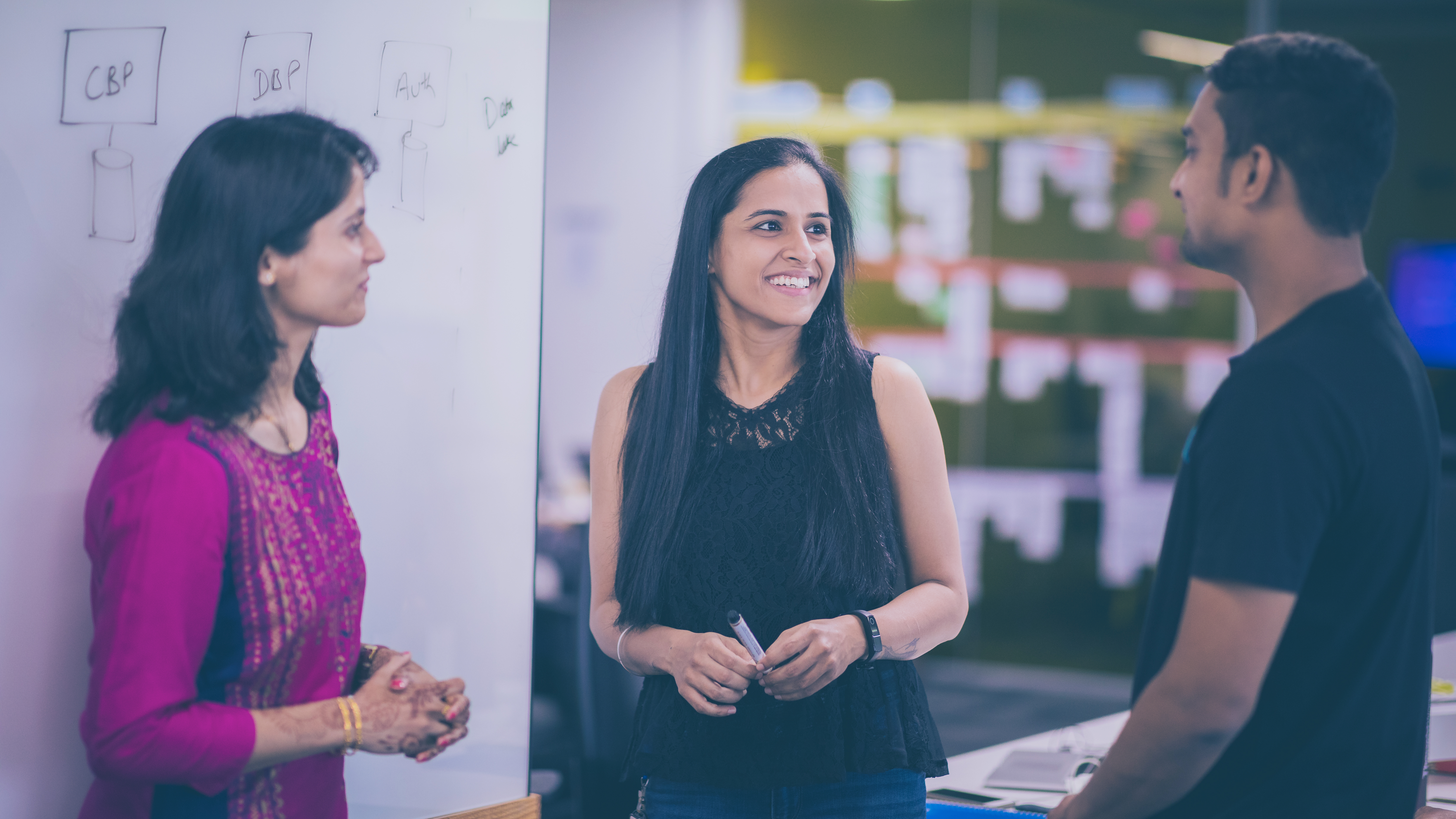 Photo of two women technologists at office speaking to a male colleague Photo of two women technologists at office speaking to a male colleague
