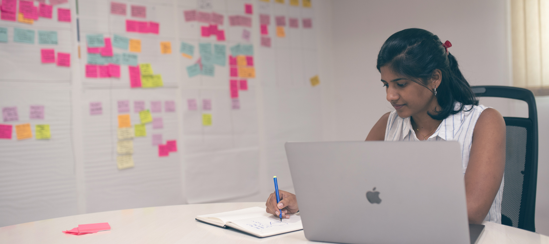 A woman working on her laptop with post notes in the background mind mapping a technical solution