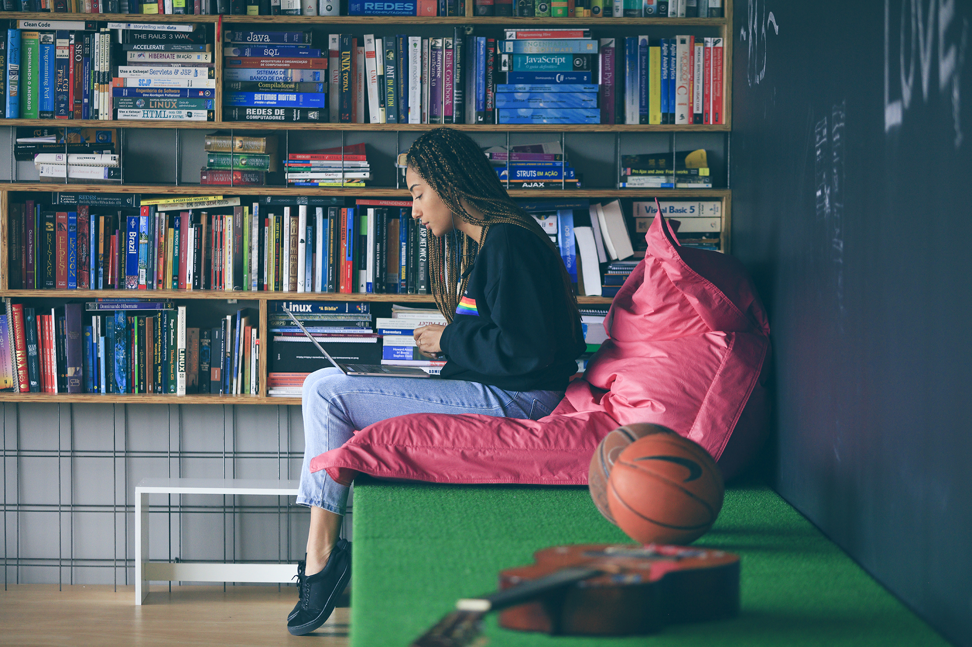 Girl relaxing by a bookshelf, looking at her laptop