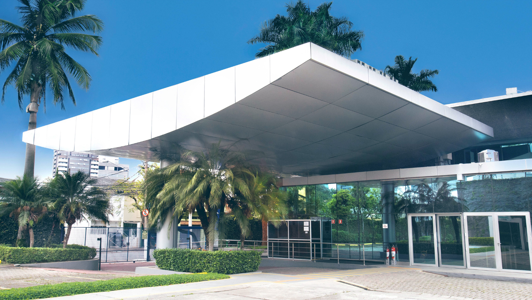 Main entrance of the American Chamber of Commerce (AMCHAM) building in São Paulo, featuring a modern glass and metal structure surrounded by palm trees and landscaped gardens Main entrance of the American Chamber of Commerce (AMCHAM) building in São Paulo, featuring a modern glass and metal structure surrounded by palm trees and landscaped gardens