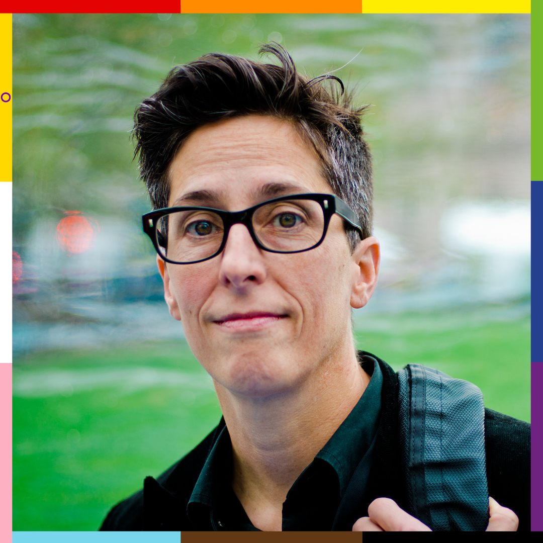 Alison, a white woman with black framed glasses, wearing a dark green shirt and black jacket, carrying a backpack  -- framed with the Pride colors