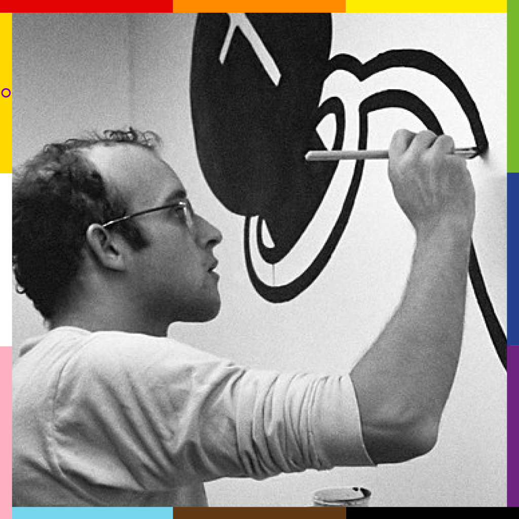 Keith, a white man in glasses is shown concentrating on a painting, framed with the progress pride flag frame