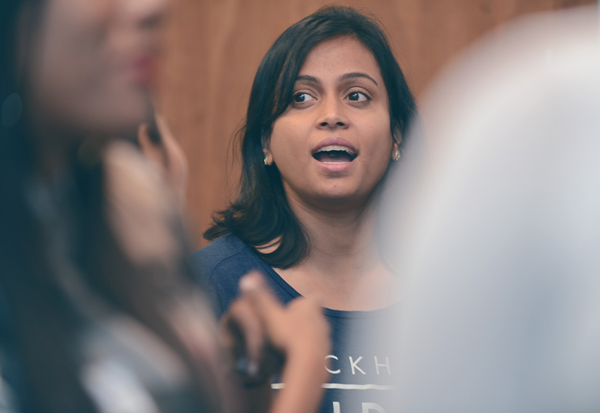 A photograph of a young south asian woman, captured during a stand up, she is talking animatedly.