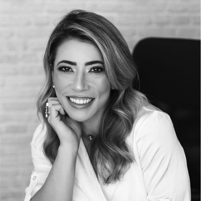 imagem-em-preto-e-branco-do-rosto-de-uma-mulher-sorrindo-morena-de-cabelos-longos-em-seu-escritorio