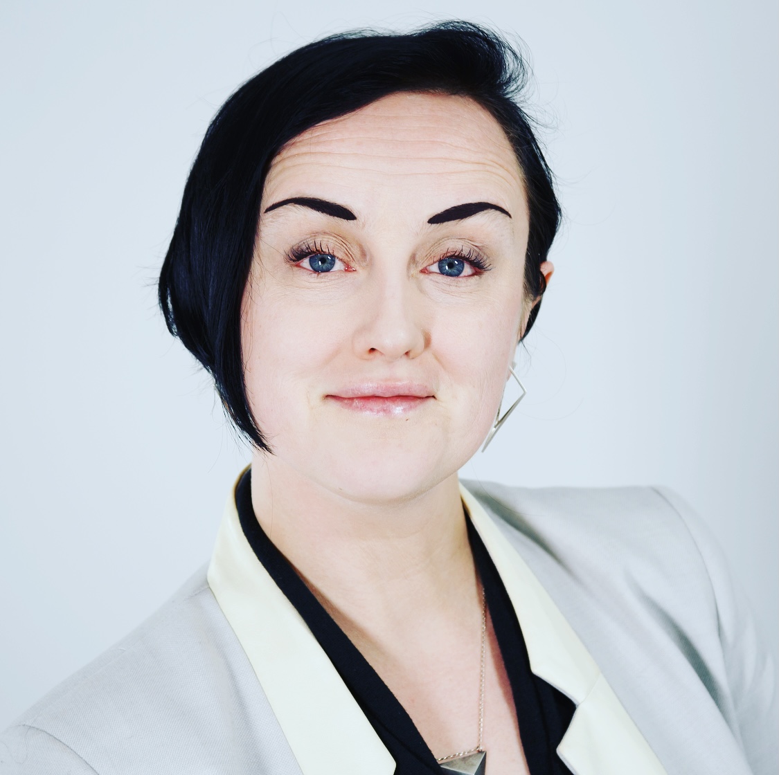 Image of Lila looking at the camera. Lila has black hair and a white suit jacket on. Image of Lila looking at the camera. Lila has black hair and a white suit jacket on.