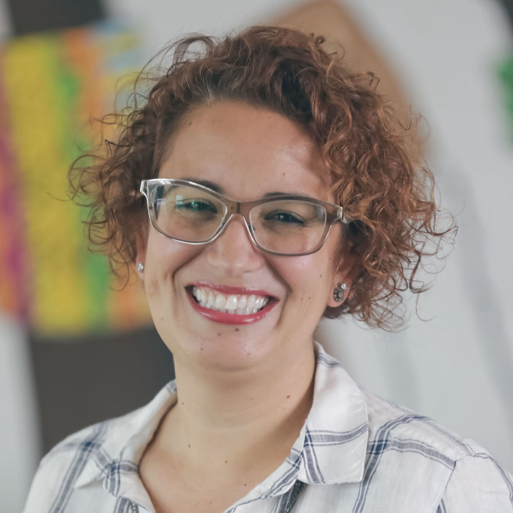 Photo of Carol Cintra, wearing glasses and smiling at the camera 