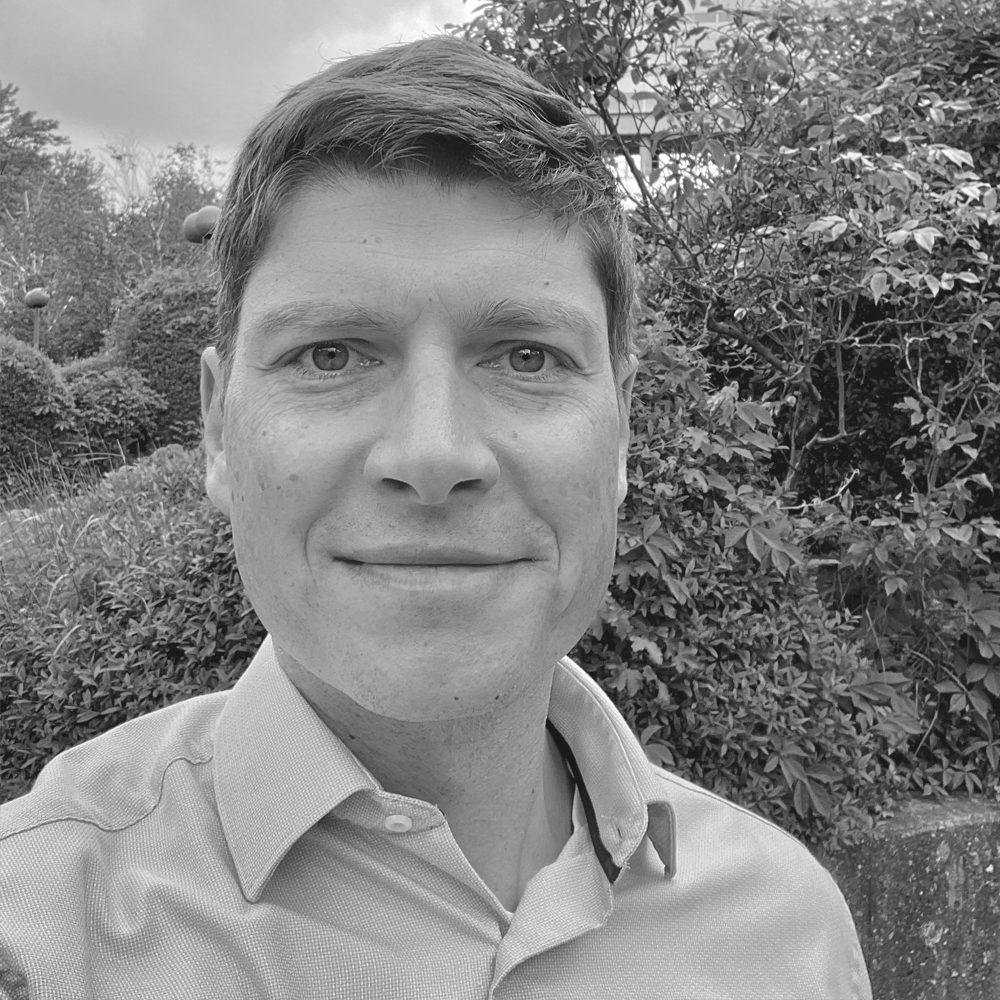 Matthias Wlaka standing in front of a hedge.