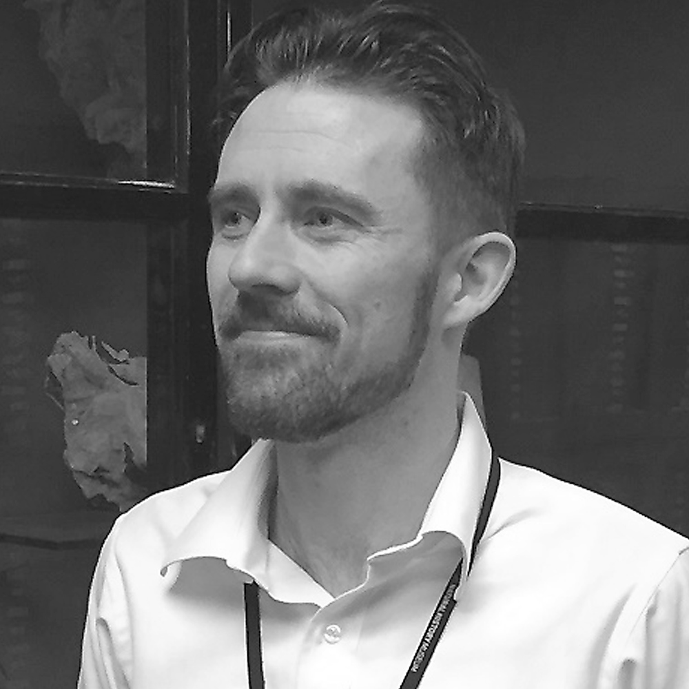 Richard Hinton wearing a white button down collared shirt and a beard.